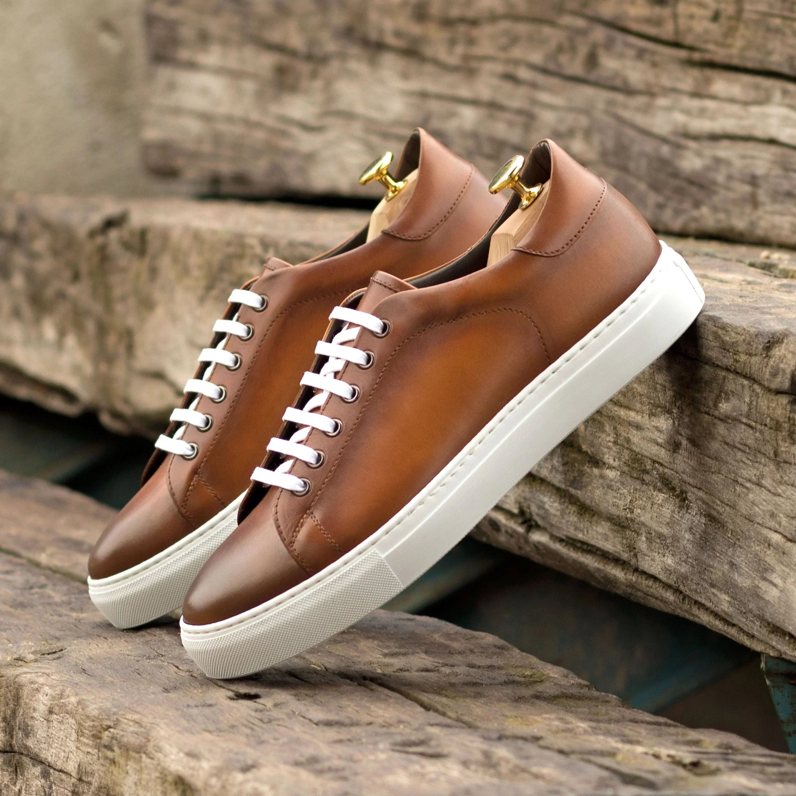 Brown leather sneakers with white laces and gold accents.